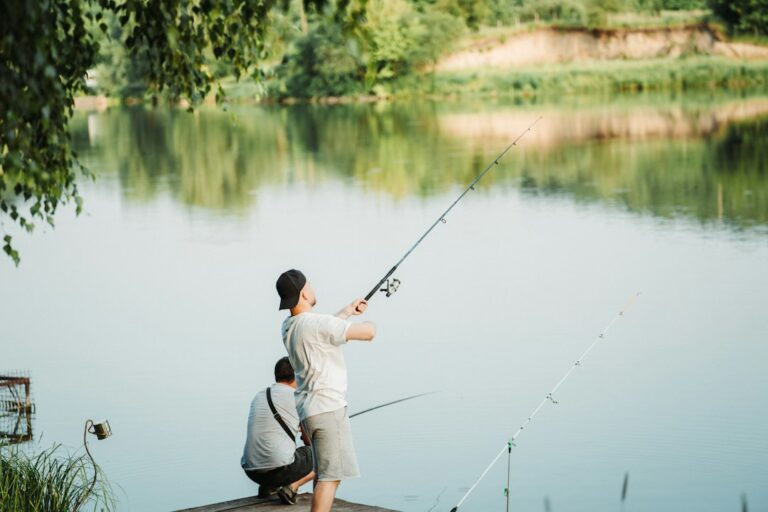An adult and child fishing together from a dock on a lake.